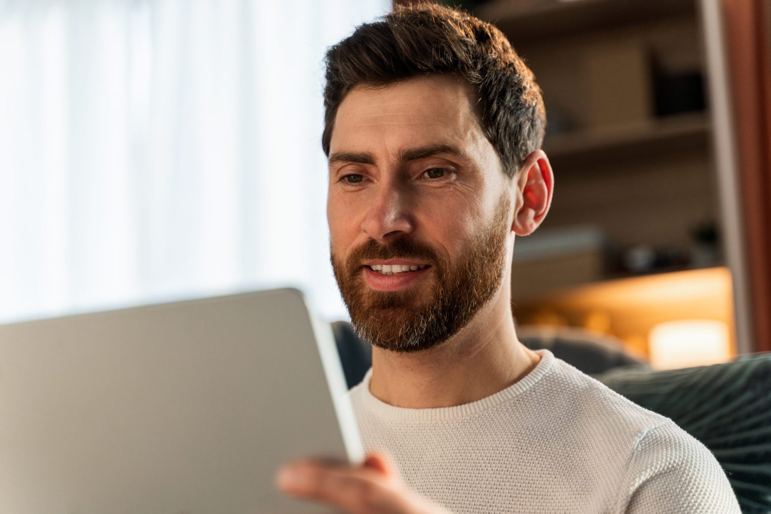 Portrait view of young man sitting on bed and looking at the tablet screen